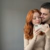 Фото пары в зеркале: рыжая девушка с белым айфоном, парень в чёрной футболке прижался к ней щекой