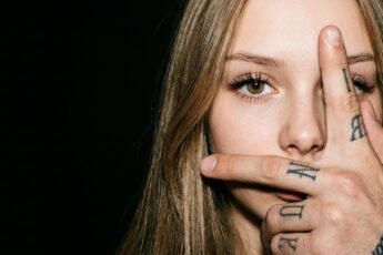 Фото глаза крупным планом: лицо девушки закрывает мужская рука с татуировками на пальцах, чёрный фон